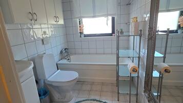 Un baño con inodoro, lavamanos, bañera y un espejo grande.