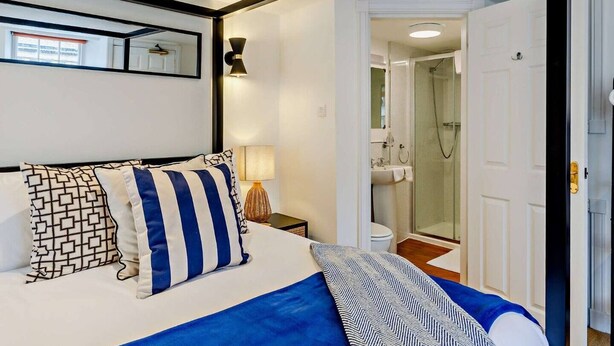 A hotel room with a bed, a bedside lamp, a mirror, and a door leading to a bathroom with a shower. - Jacobite's Retreat, 17th century cottage (Inverness)
