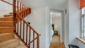 A staircase with wooden railings leading to a bedroom with a green headboard and a bedside table with a lamp. - Jacobite's Retreat, 17th century cottage (Inverness)