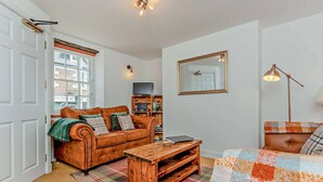 A cozy living room with a brown leather sofa, a wooden coffee table, and a colorful blanket. - Jacobite's Retreat, 17th century cottage (Inverness)