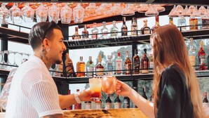 Angolo bar con sedie in vimini e un tavolo, e diverse bottiglie di liquore sugli scaffali dietro il bancone.