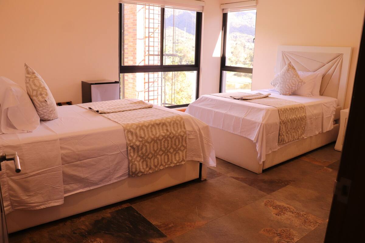 A hotel room with two beds, large windows, and a view of the outdoors.