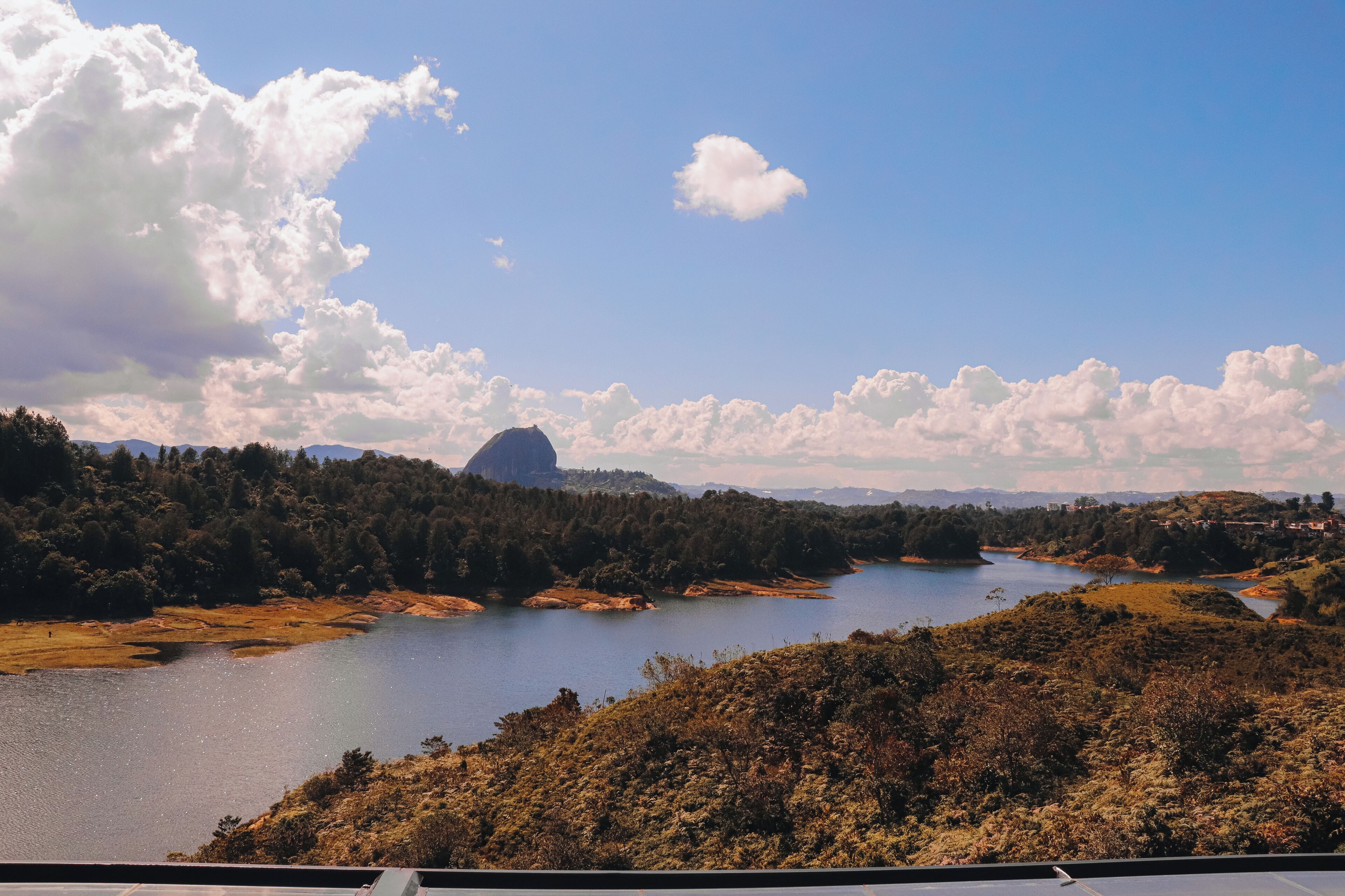 A scenic landscape with a lake, forested hills, and a prominent mountain in the distance.