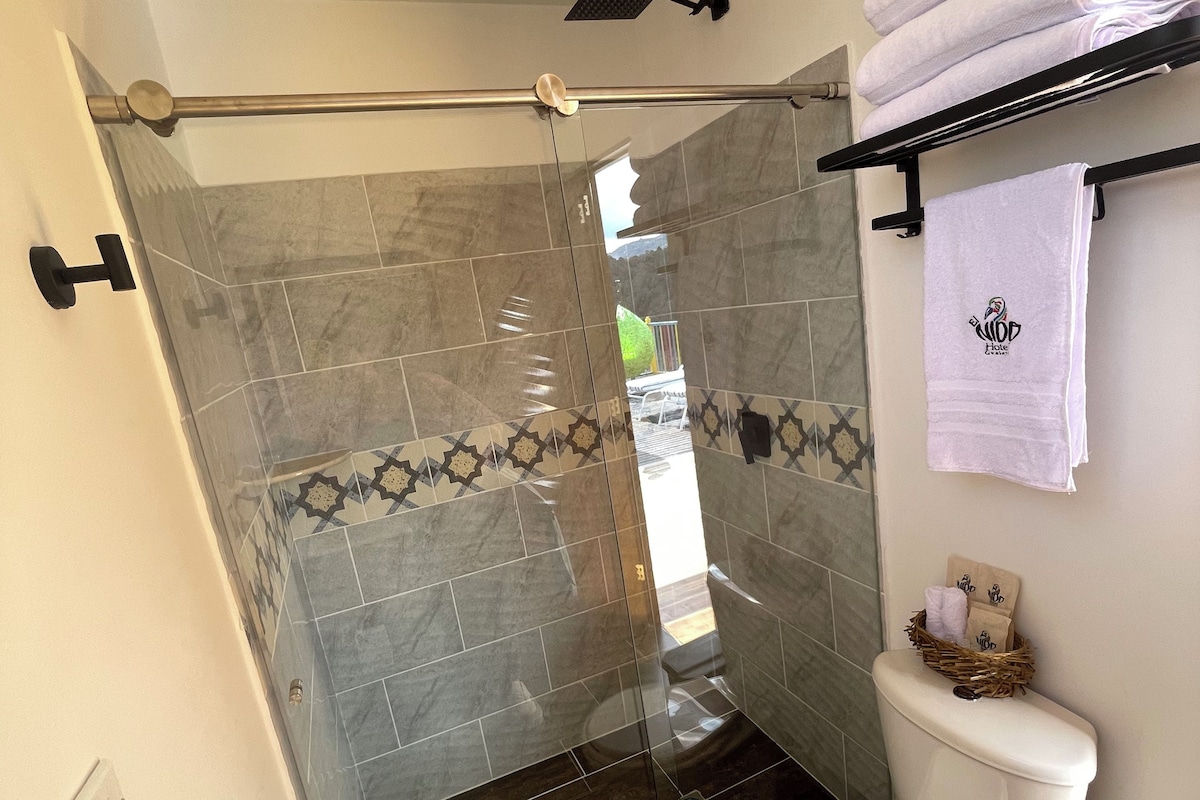 A bathroom with a glass shower enclosure, a toilet, and a towel rack with folded towels.