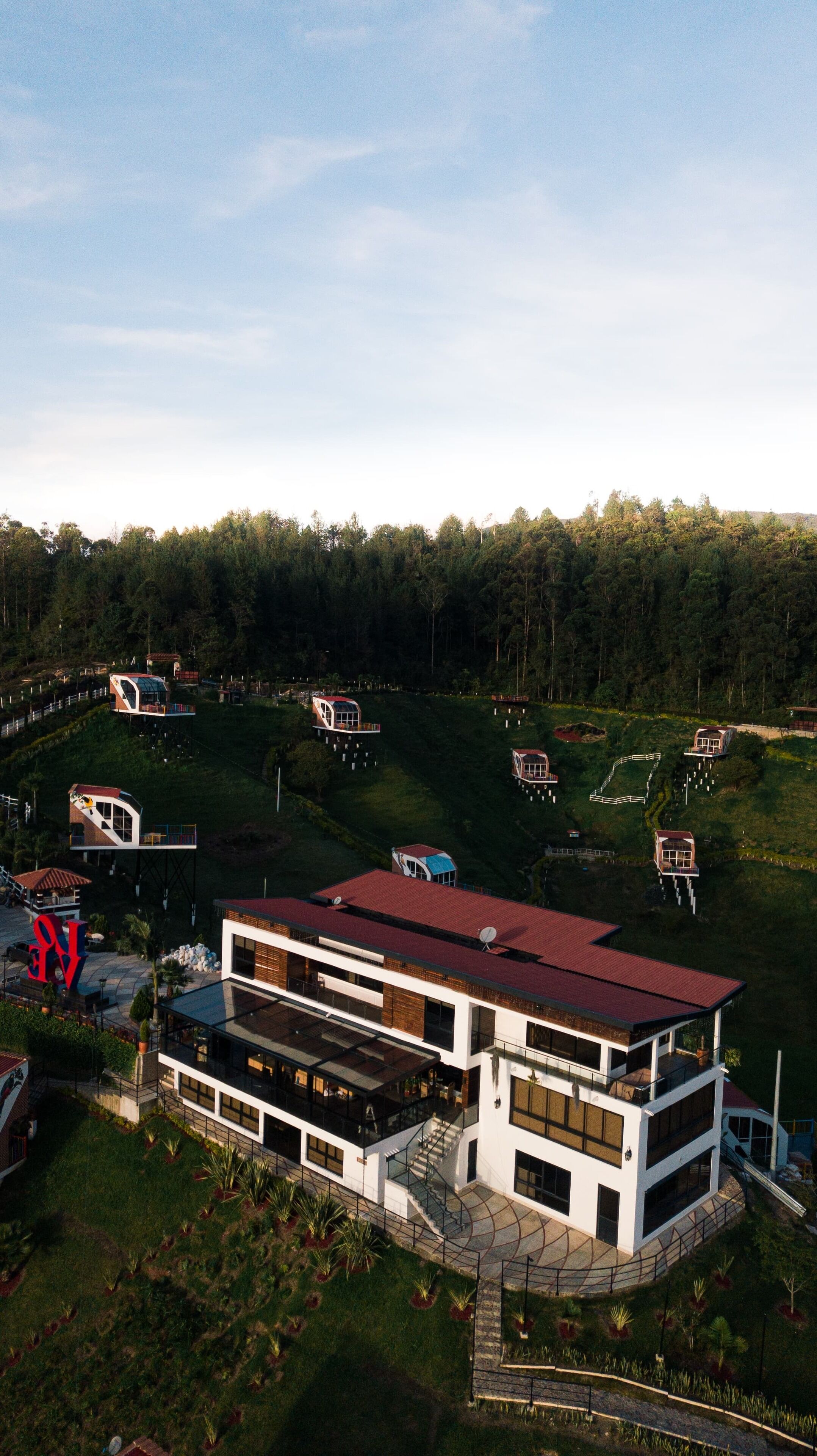 A modern multi-story house with a red roof, surrounded by a forested area.