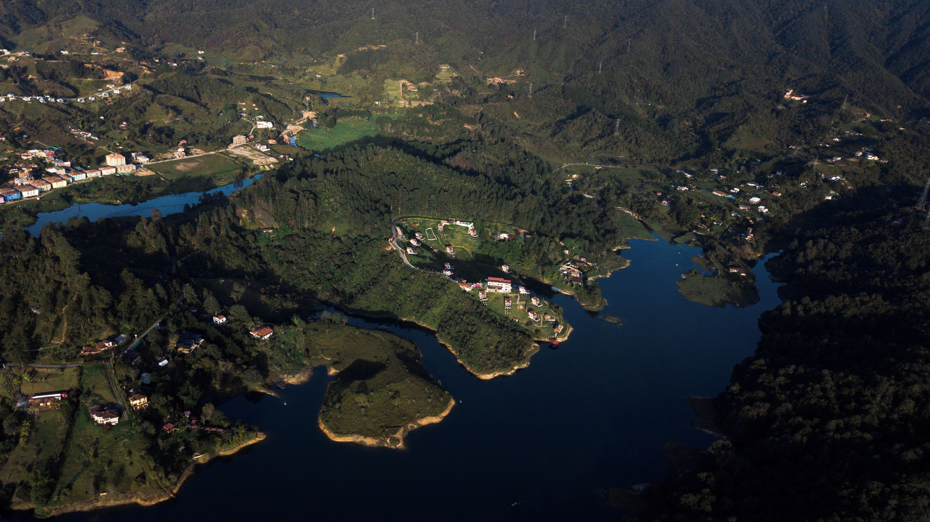 Une vue aérienne d’une zone côtière avec un petit village, comprenant des maisons et des bâtiments situés près de l’eau, le tout entouré d’une forêt dense.