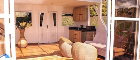 Un interior moderno con piso de madera, muebles de mimbre, una zona de cocina y ventanas amplias.