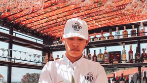Un barista all'Hotel El Nid, che tiene uno shaker per cocktail e un drink. Dietro di lui, scaffali pieni di diverse bottiglie di liquore.