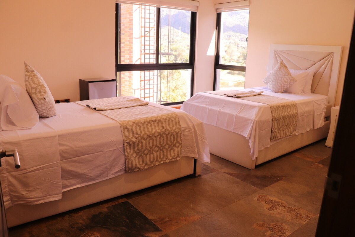 Habitación de hotel con dos camas, ventanas amplias y vista al exterior.
