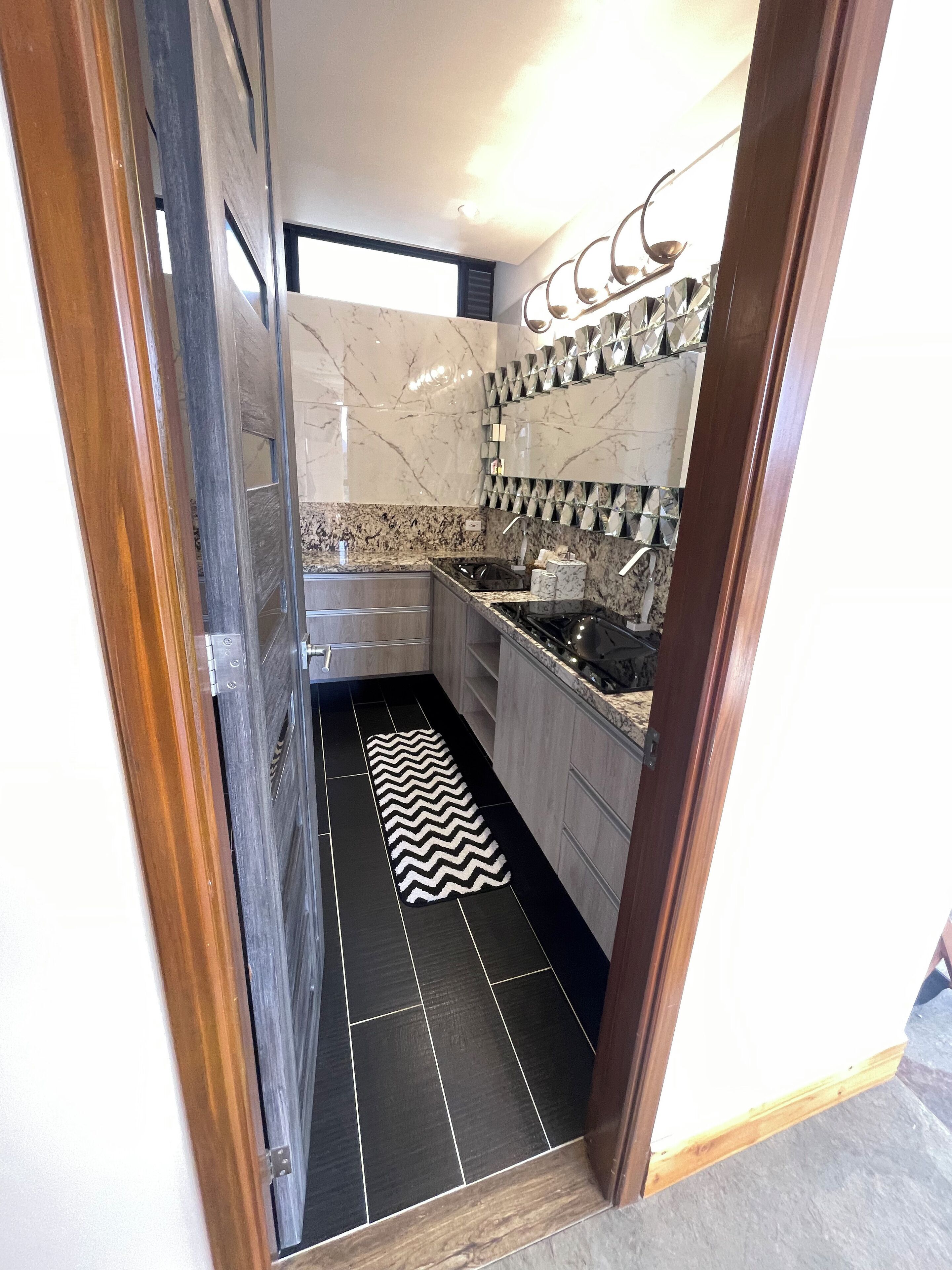 A modern kitchen with dark tiles, a black and white rug, and a marble backsplash.