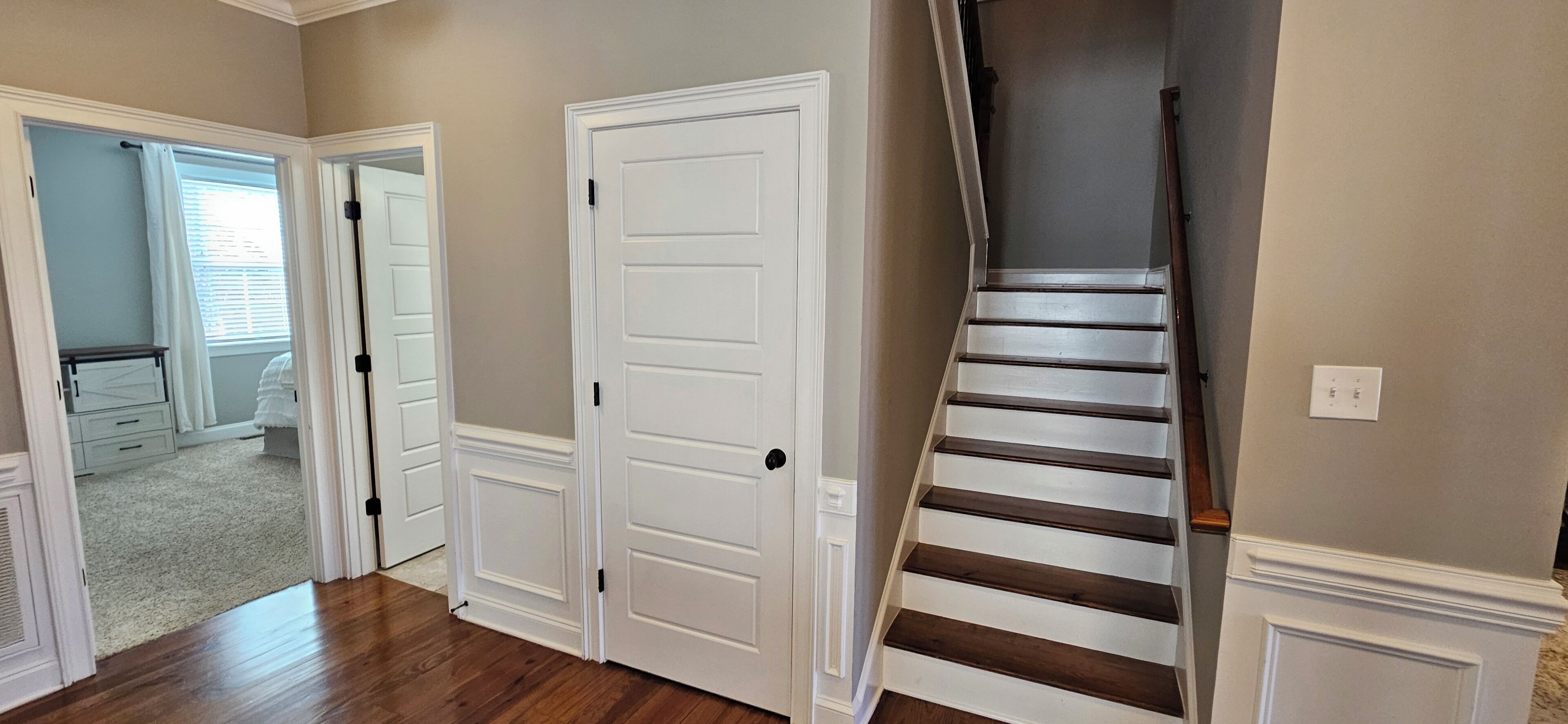 A hallway with a wooden floor, a white door, and a staircase with dark wood steps.