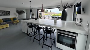 Een moderne keuken met een centraal eiland, zwarte barkrukken, een ingebouwde oven en hanglampen.