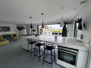Een moderne keuken met een centraal eiland, zwarte barkrukken, een ingebouwde oven en hanglampen.