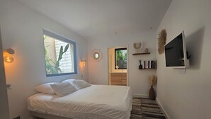 Een slaapkamer met een bed, een raam, een televisie en een zichtbare badkamer op de achtergrond.