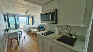 A compact, modern room with a kitchenette, a bed, a dining area, and a view of the sea.