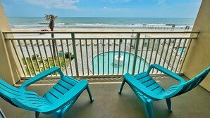 A balcony with two turquoise lounge chairs, a pool, and a view of the beach and ocean.