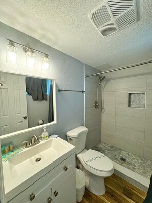 A bathroom with a white sink, mirror, and toilet, a shower with a glass door, and a tiled floor.
