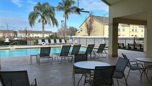 A poolside area with lounge chairs and tables, a pool, palm trees, and a view of residential buildings. - ★12Mins to Disney Theme Parks- Save 25pct Off Stay- Pool- 3BR Condo-Sleeps 10★ (Kissimmee)