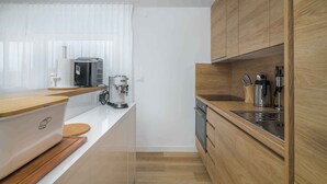 Moderni keittiö, jossa on puiset kaapit, valkoinen työtaso, kahvinkeitin ja astianpesukone.