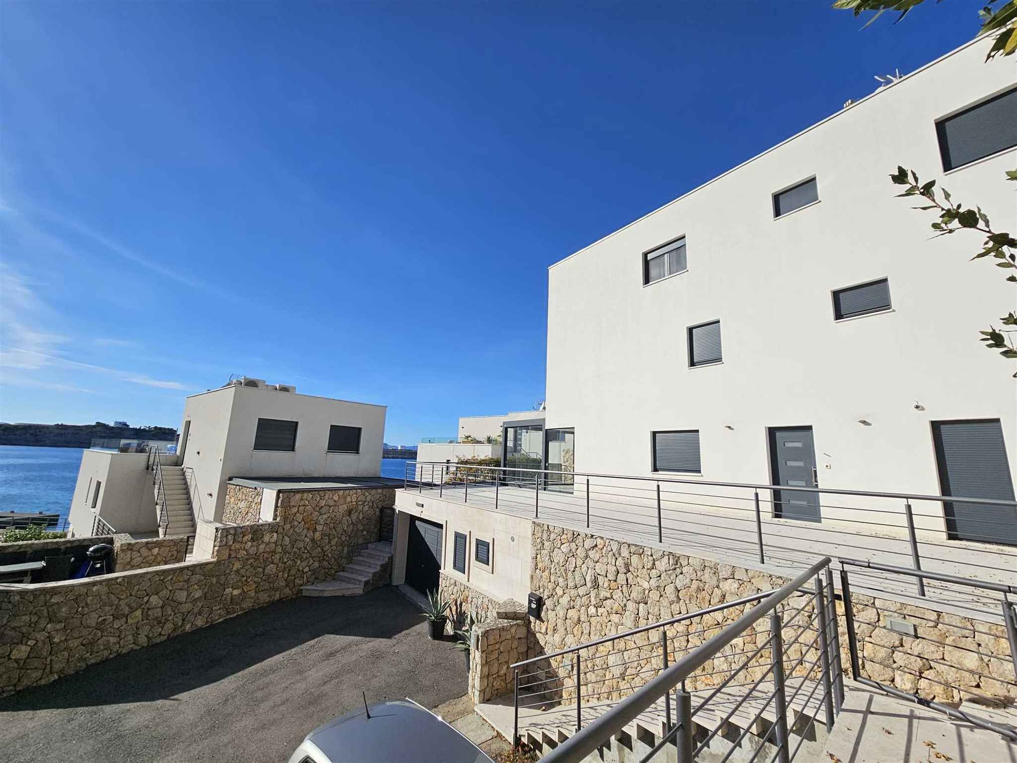 A modern building with a stone facade, a staircase leading to a flat roof, and a view of the sea.