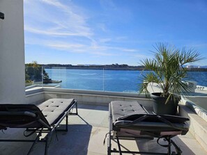 Un balcon avec deux fauteuils et un pot de fleurs, dâoĂč lâon peut admirer un plan dâeau et un paysage lointain.