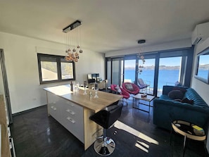 Une cuisine moderne avec un ßlot central, un coin repas avec des chaises, un canapé et une vue sur la mer.