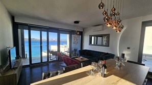 Ein modernes Wohnzimmer mit einem großen Holzesstisch, einer Couch und Meerblick durch große Fenster.