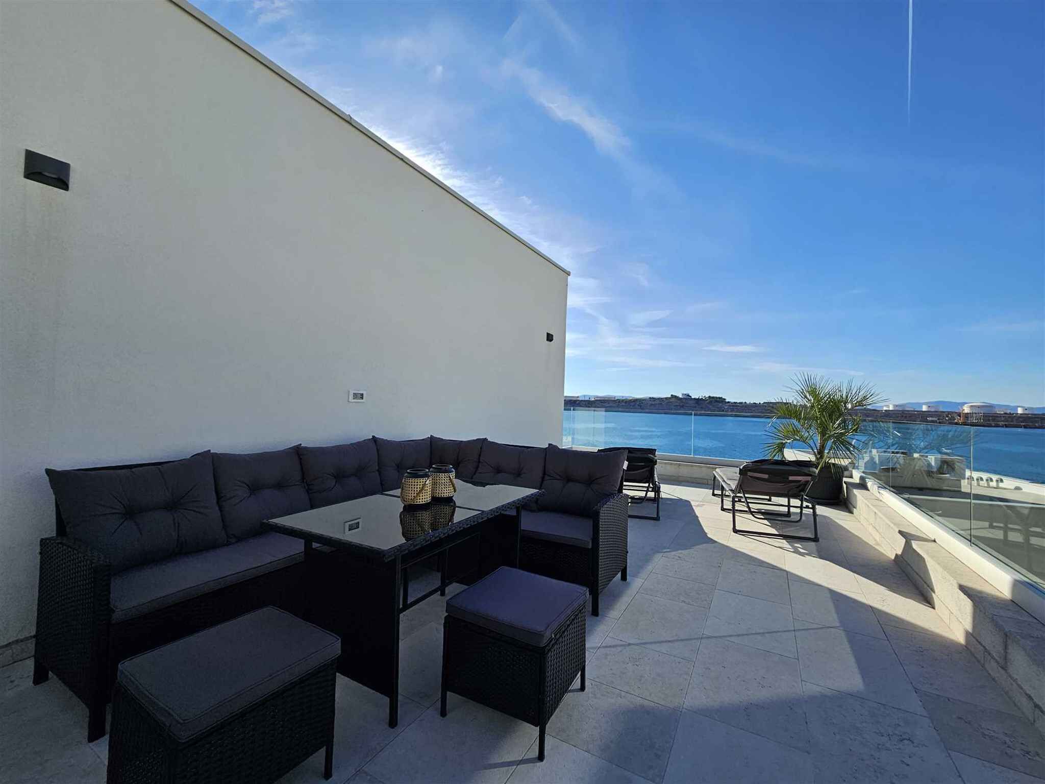 Eine Dachterrasse mit Sofa, Tisch, Stühlen und Meerblick.
