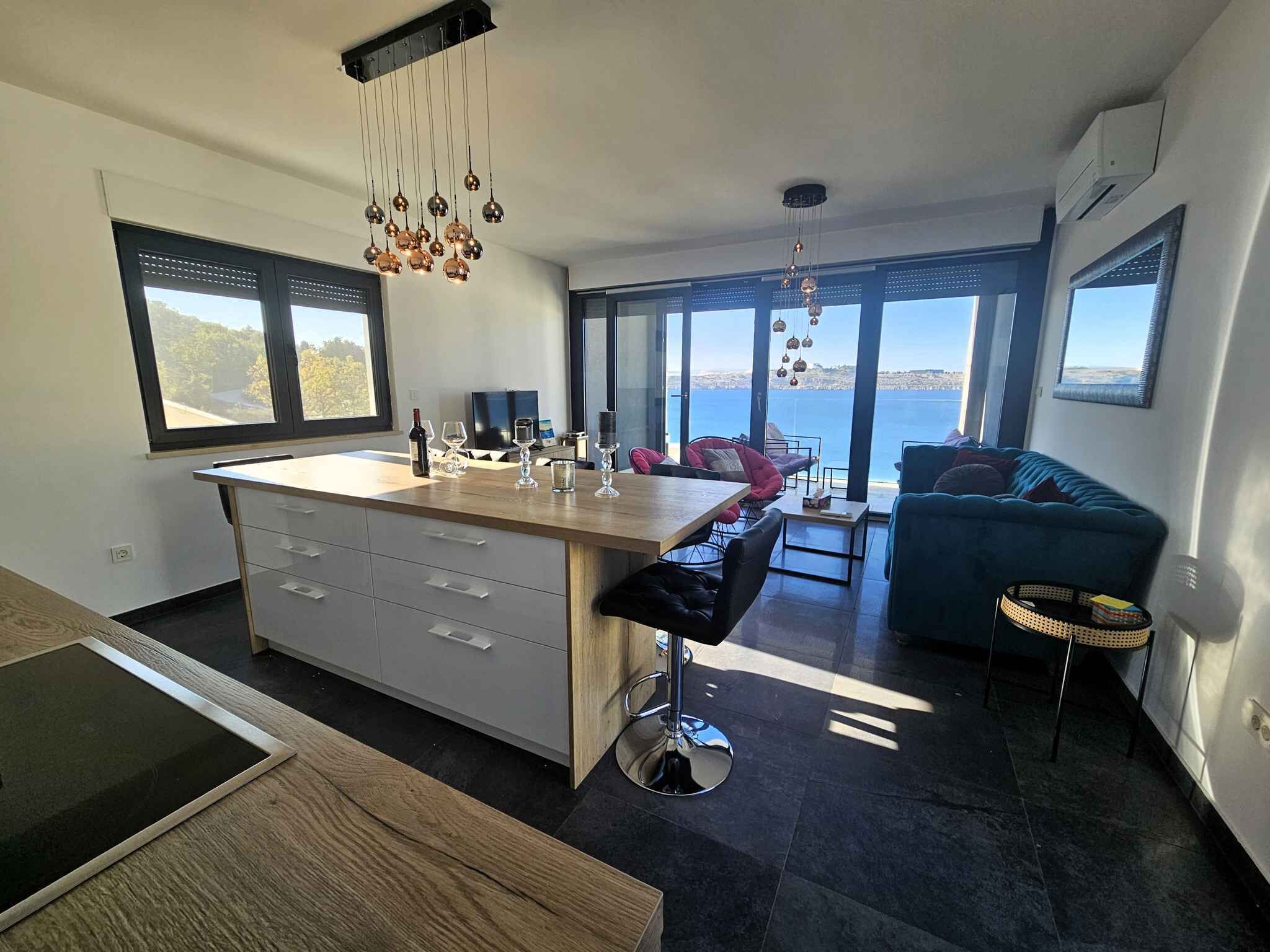 A modern kitchen with a central island, bar stools, and a view of the sea.