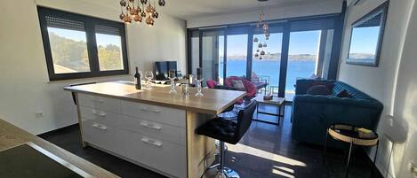 A modern kitchen with a central island, bar stools, and a view of the sea.