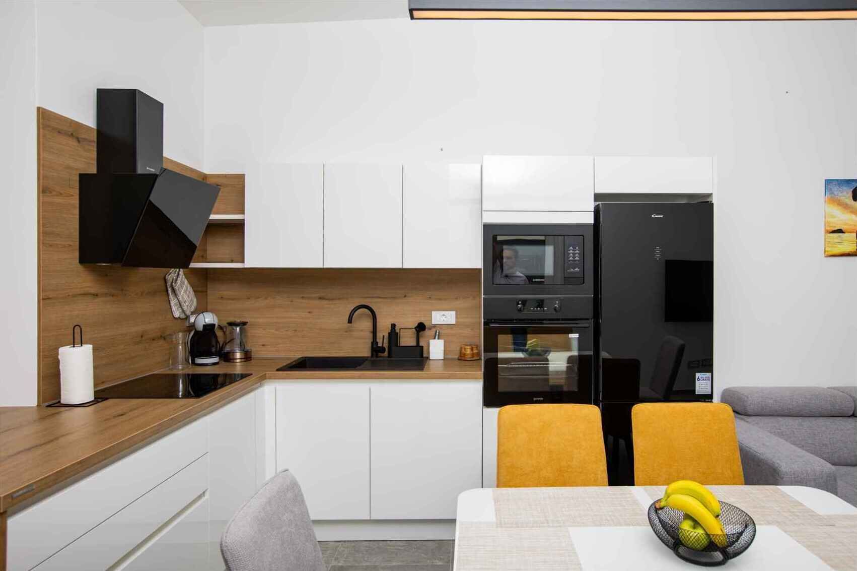 A modern kitchen with white cabinets, a black refrigerator, and a microwave. There is a dining area with a table and chairs, and a painting on the wall.