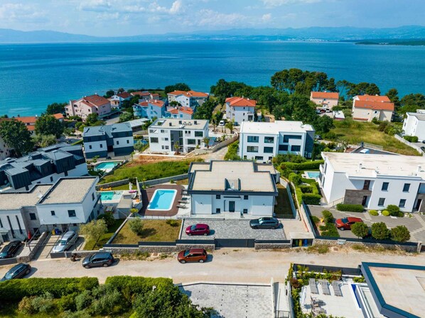 A coastal residential area with modern houses, a swimming pool, and a view of the sea.