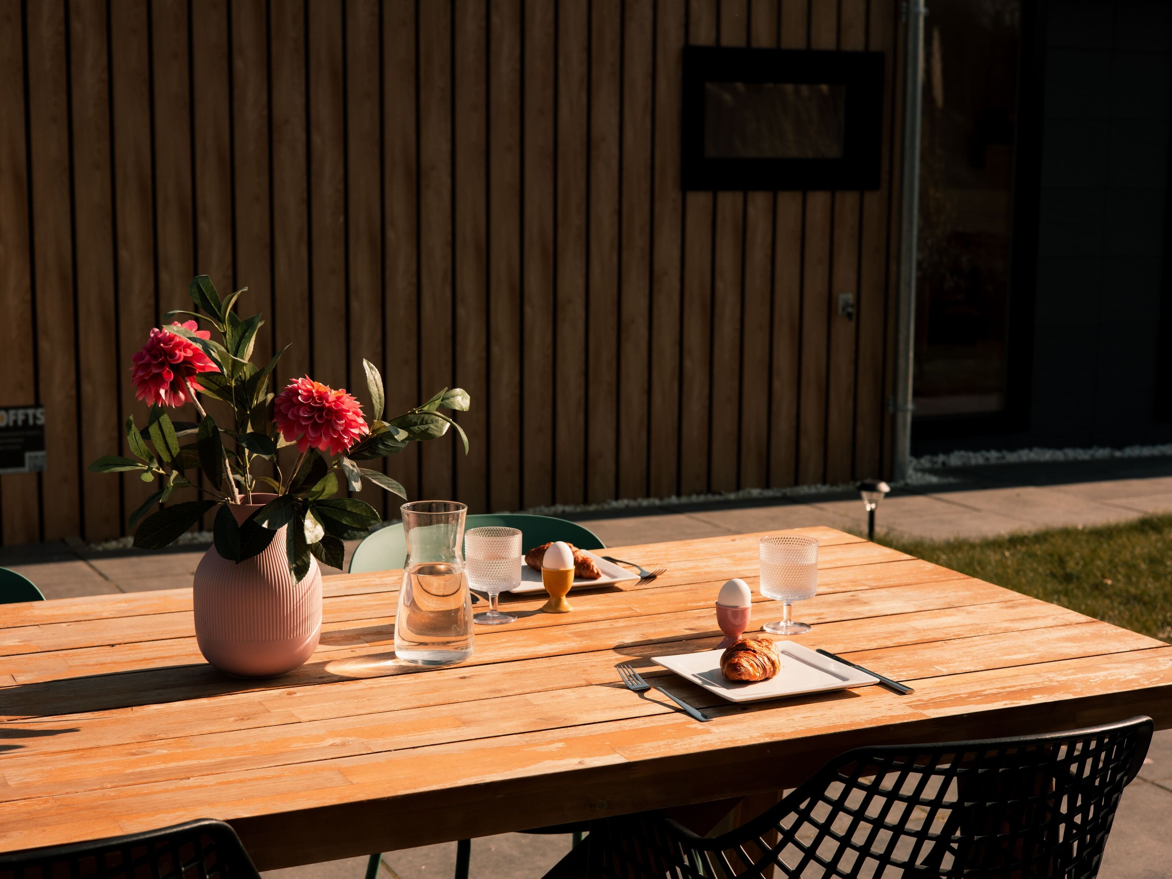 Ein Holztisch mit einer Blumenvase, einem Glas Wasser, einem Croissant und einem Teller mit einem Croissant.