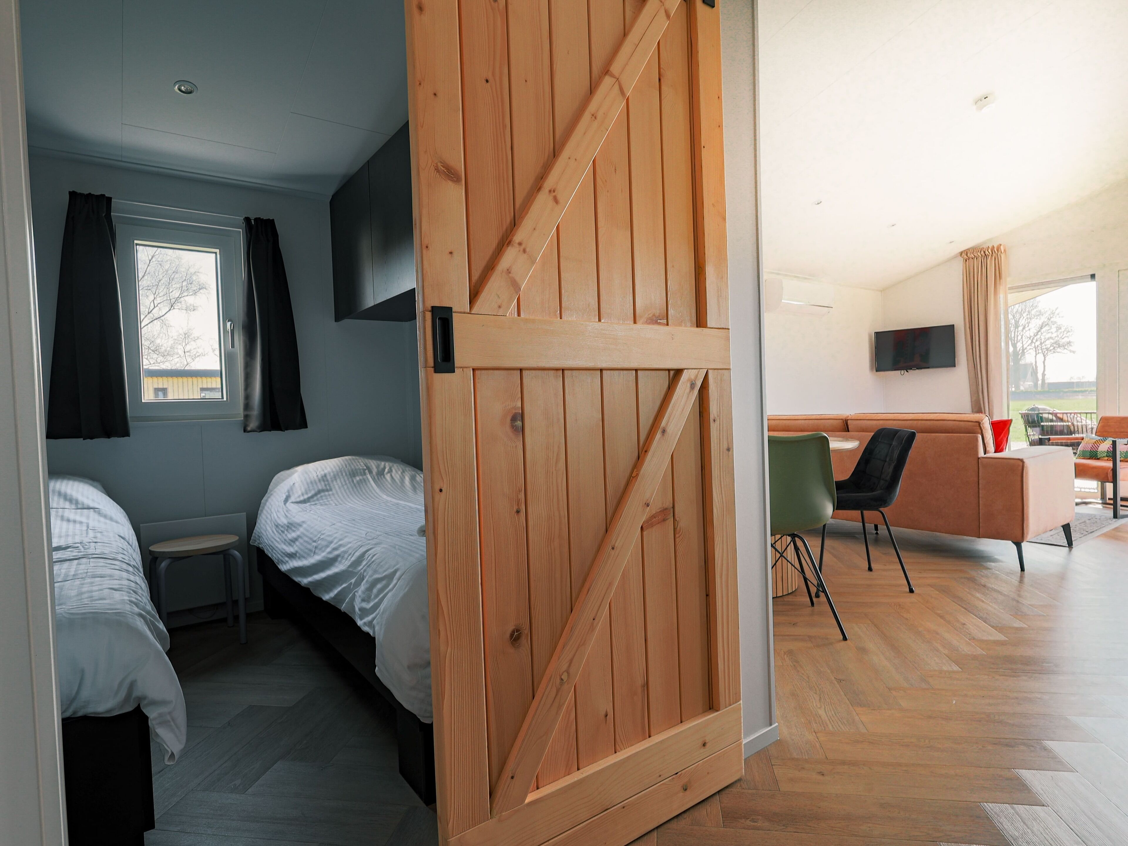Ein Zimmer mit zwei Betten, einer Holztür, die sich verschieben lässt, einem an der Wand montierten Fernseher und Blick ins Freie.