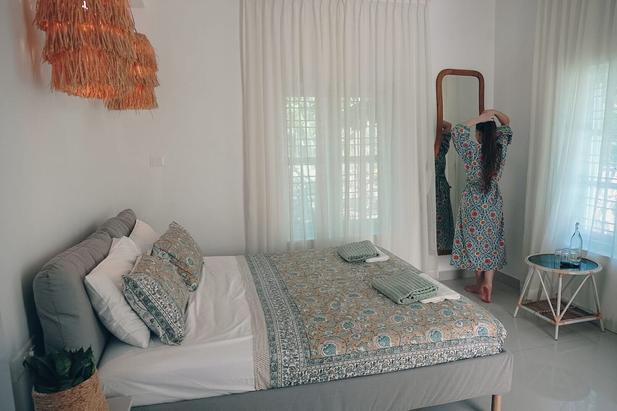 A bedroom with a bed, a mirror, a small table, and a potted plant.