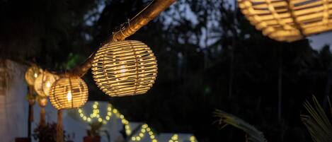 Outdoor lighting fixtures with a warm glow, string lights, and potted plants.