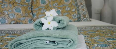 A neatly folded green towel with a white flower on a bed with a patterned bedspread.