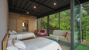 Een slaapkamer met twee bedden, een bank en een glazen deur die leidt naar een balkon met uitzicht op groen.