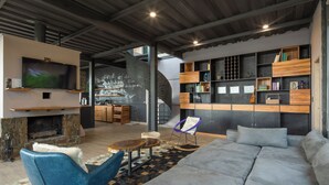 Een moderne woonkamer met een stenen open haard, een grote flatscreen televisie, een grijze bank, een blauwe fauteuil en een houten boekenkast.