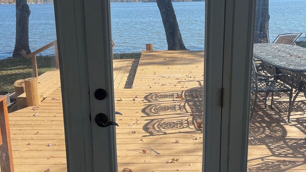 Een houten terras met een tafel en stoelen, met uitzicht op een meer met bomen en een verre oever.