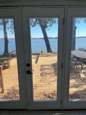 Une terrasse en bois avec une table et des chaises, donnant sur un lac bordé d’arbres et dont on aperçoit la rive au loin.