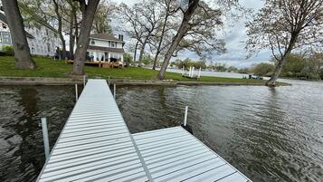 A wooden dock extending into a body of water with a house and trees in the background.