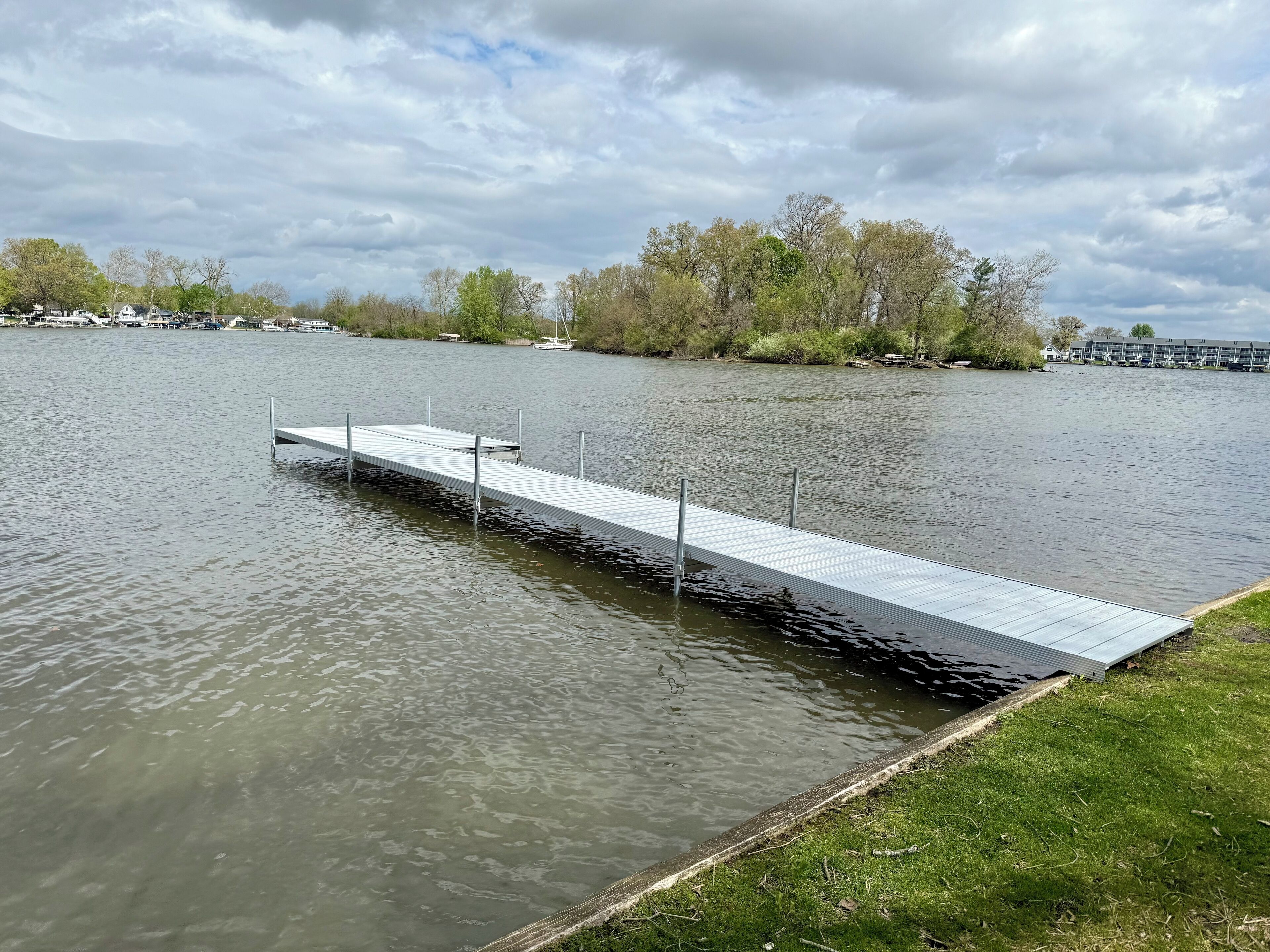 Une jetée s’avançant dans un lac paisible, avec une rive herbeuse d’un côté.