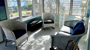 Een knus ingerichte kamer met uitzicht op het water, met rieten meubels, een vloer met patroon en een bordje 'Summer'.
