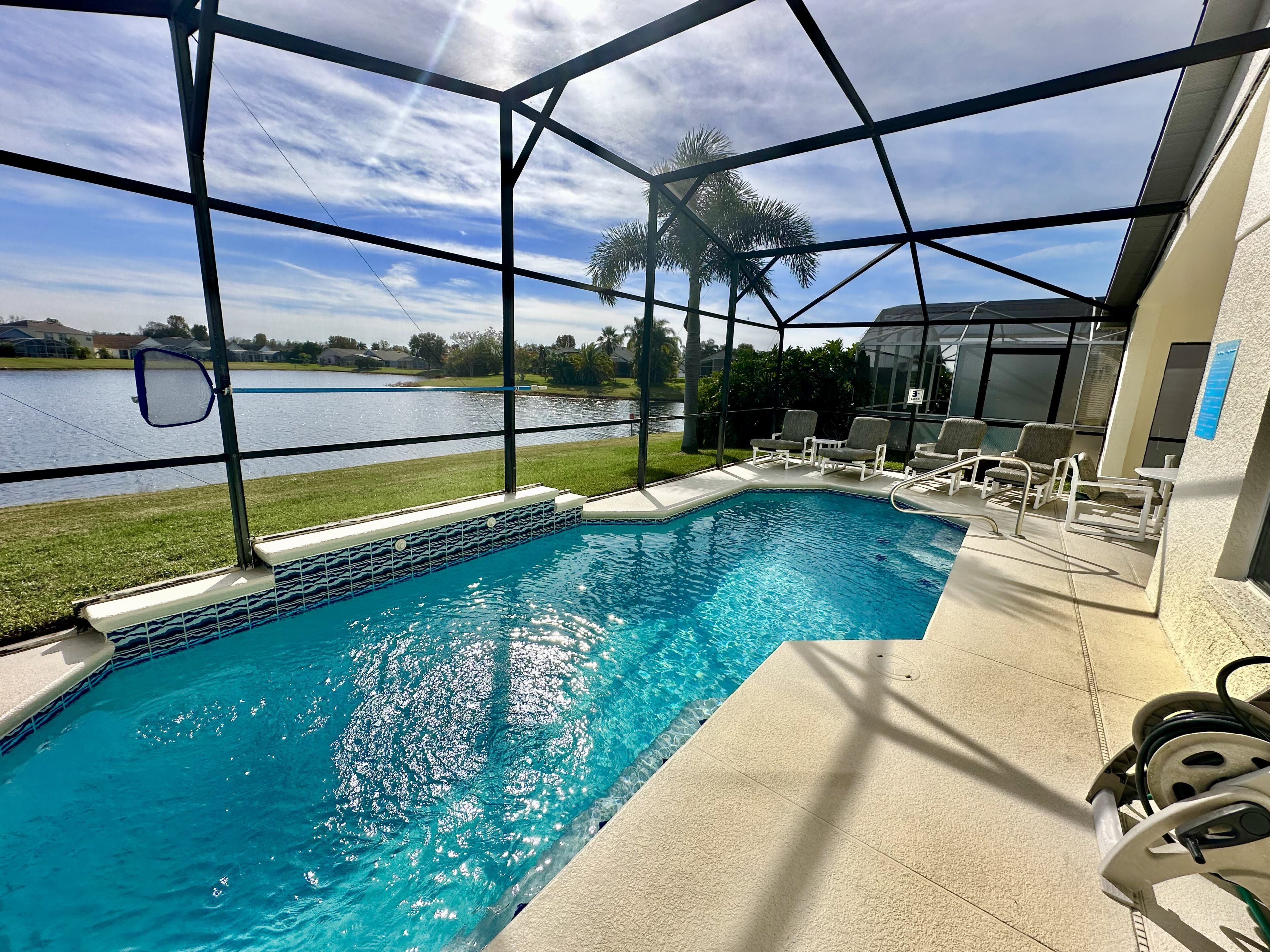 A swimming pool with a view of a lake, surrounded by a covered area with chairs and a table.