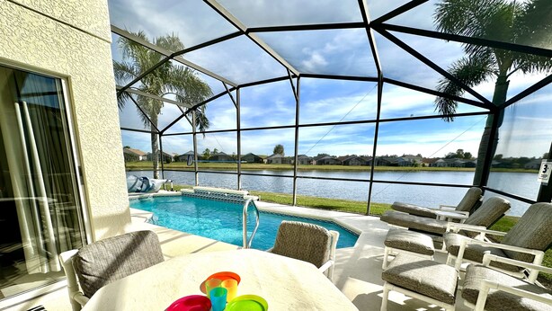 Zona junto a la piscina con vista a un lago, mobiliario exterior y un porche cubierto.