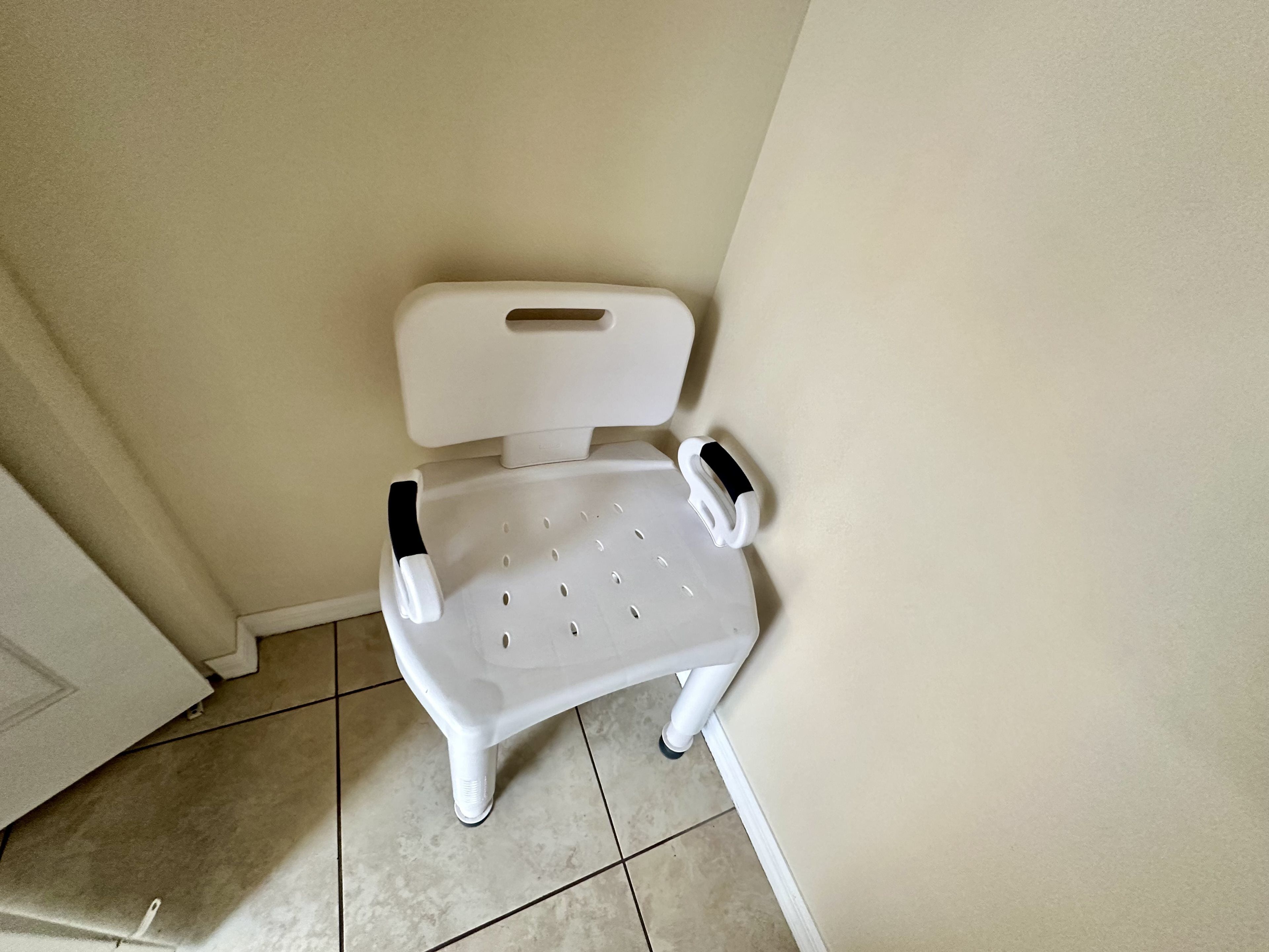 A white plastic chair with armrests and a footrest, positioned against a wall in a room with tiled flooring.