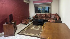A living room with a sofa, a coffee table, a TV stand, and a dining table. - 2-bedroom Furnished apartment for rent in the heart of 
 jabal amman (Amman)