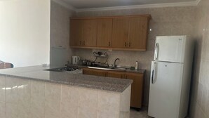 A kitchen with granite countertops, wooden cabinets, a white refrigerator, and a gas stove. - 2-bedroom Furnished apartment for rent in the heart of 
 jabal amman (Amman)