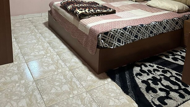 A bedroom with a large bed, a window, a nightstand, and a patterned rug. - 2-bedroom Furnished apartment for rent in the heart of 
 jabal amman (Amman)